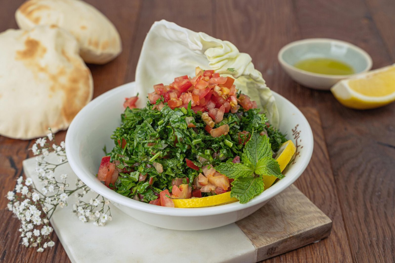 Vibrant tabbouleh salad with fresh ingredients, served with pita bread and lemon wedges.